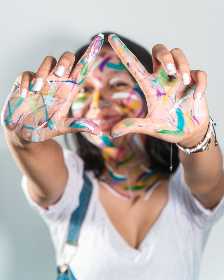 A young woman creatively expresses herself with paint on her face and hands.